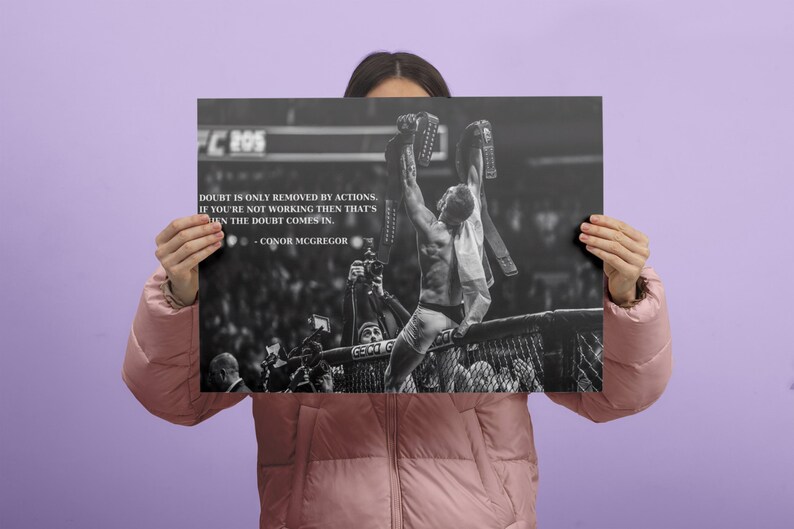 May include: Black and white poster featuring a victorious athlete holding championship belts. The poster includes the text "Doubt is only removed by actions. If you're not working then that's when the doubt comes in." by Conor McGregor.