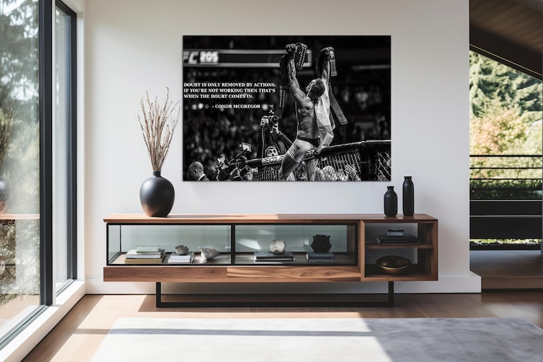 May include: Black and white framed print featuring a victorious athlete raising his arms. The print includes text: "Doubt is only removed by actions. If you're not working then that's when the doubt comes in." A modern, wooden media console is below.