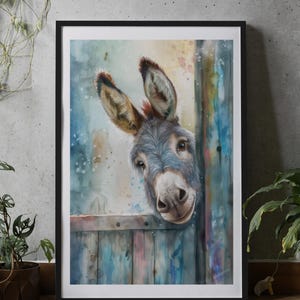 May include: A framed watercolour painting of a donkey looking over a wooden fence. The donkey has grey fur and large ears. The background is a colourful wash of blues, greens, and pinks. The artwork is framed in a black frame.