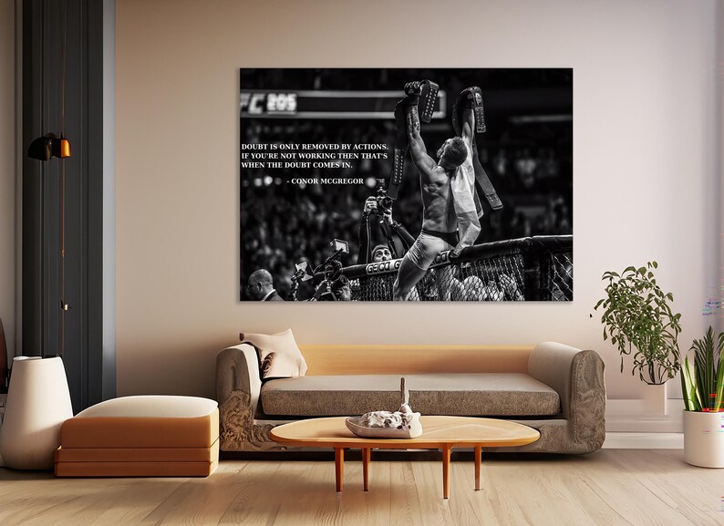 May include: Black and white print of a victorious athlete holding up championship belts. The image includes the quote "Doubt is only removed by actions. If you're not working then that's when the doubt comes in." by Conor McGregor.