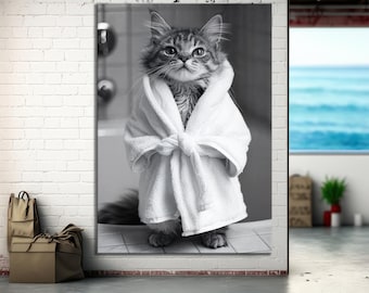 May include: A black and white image of a fluffy cat wearing a white terry cloth robe. The cat is sitting upright, looking directly at the viewer. The robe is tied at the waist, and the cat appears to be in a bathroom setting.