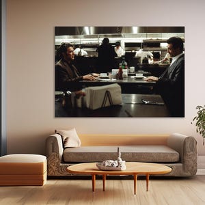 May include: A framed print of a scene from a movie, depicting two men seated at a table in a restaurant. The background shows the kitchen staff at work. The room is decorated with a sofa, a coffee table, and a floor lamp.
