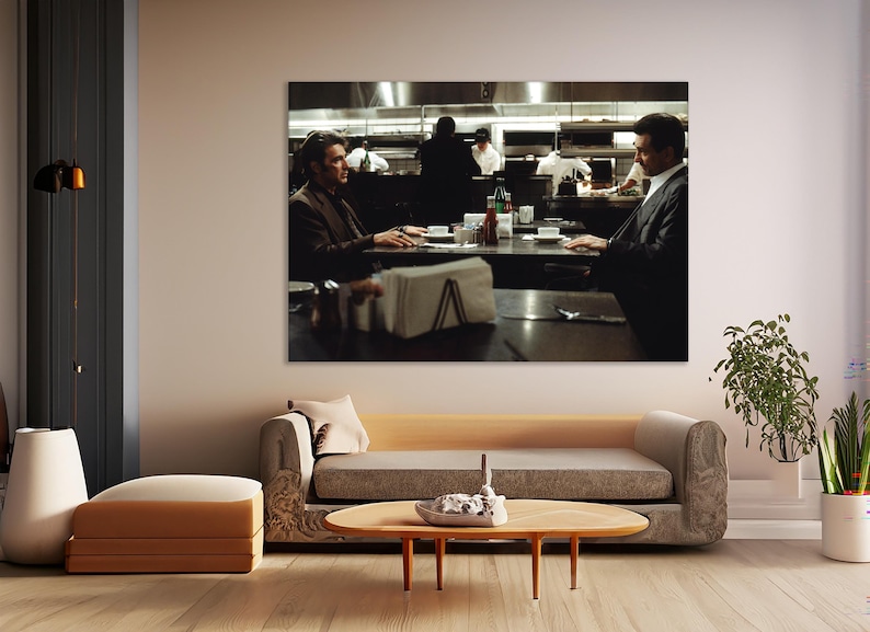 May include: A framed print of a scene from a movie, depicting two men seated at a table in a restaurant. The background shows the kitchen staff at work. The room is decorated with a sofa, a coffee table, and a floor lamp.