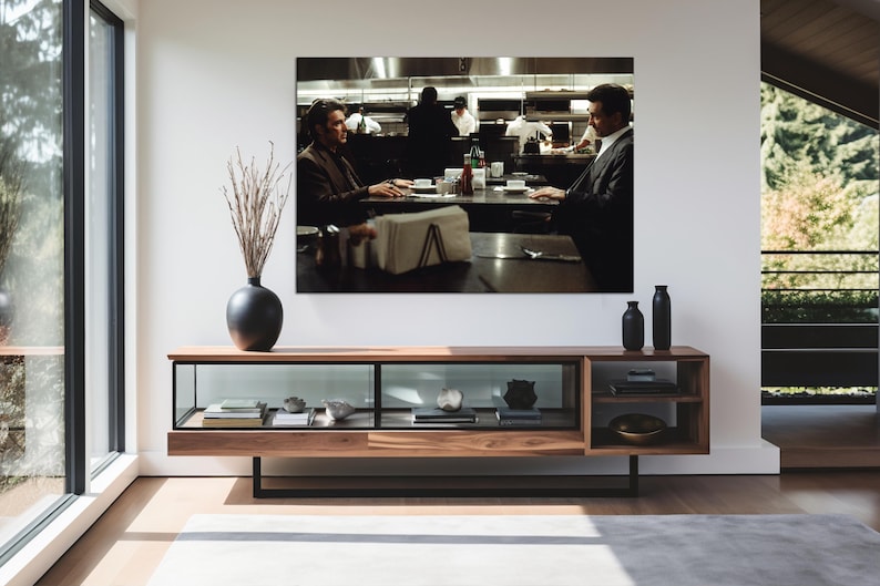 May include: A large framed print of a movie scene hangs above a modern wooden console table. The table has a glass-fronted cabinet and open shelves. A black vase with dried branches and two black bottles are on the table.
