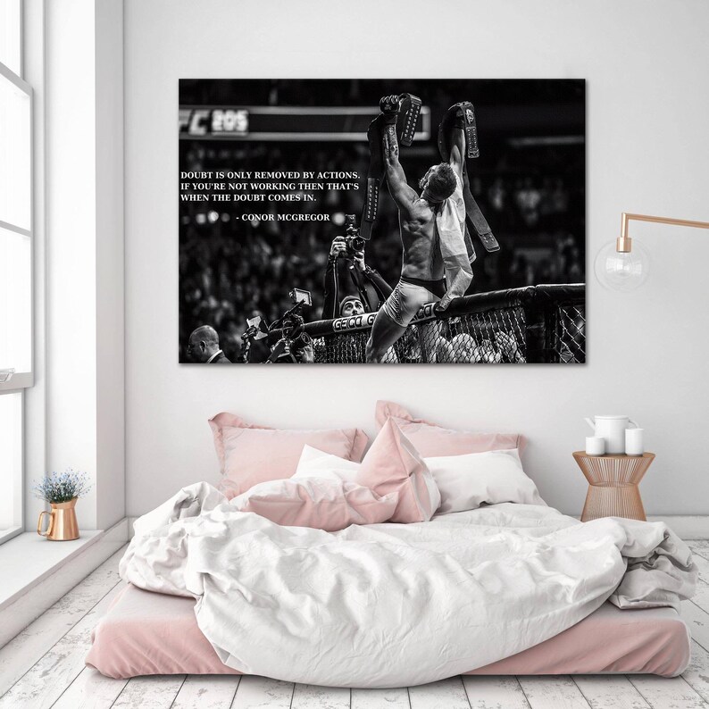 May include: Black and white print of a victorious athlete holding up championship belts. The image includes text that reads "Doubt is only removed by actions. If you're not working then that's when the doubt comes in." - Conor McGregor.
