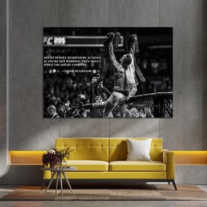 May include: Black and white framed print featuring a victorious athlete holding championship belts. The print includes the text "DOUBT IS ONLY REMOVED BY ACTIONS. IF YOU'RE NOT WORKING THEN THAT'S WHEN THE DOUBT COMES IN. - CONOR MCGREGOR."