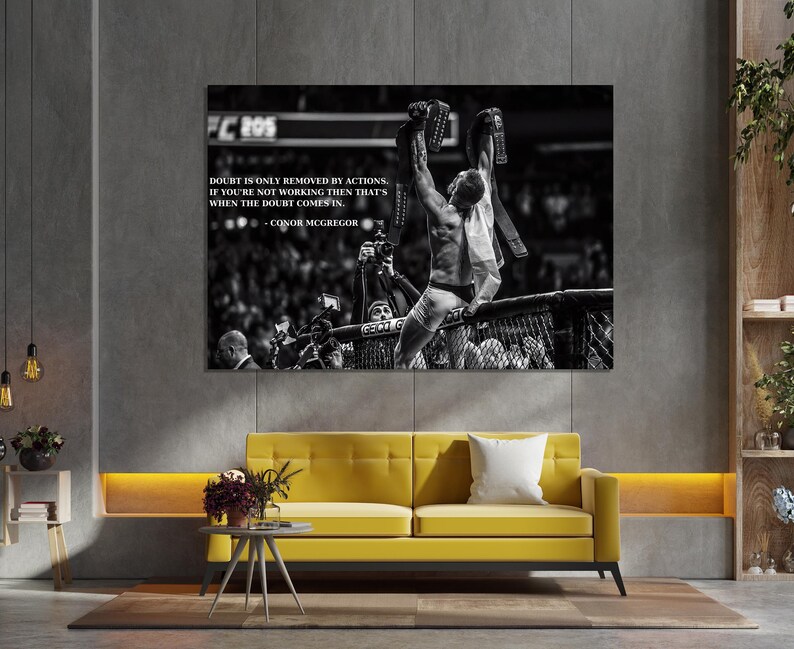 May include: Black and white framed print featuring a victorious athlete holding championship belts. The print includes the text "DOUBT IS ONLY REMOVED BY ACTIONS. IF YOU'RE NOT WORKING THEN THAT'S WHEN THE DOUBT COMES IN. - CONOR MCGREGOR."