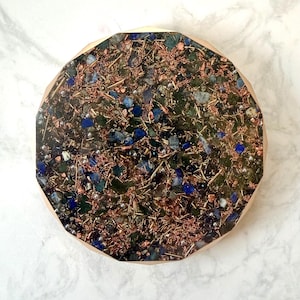 May include: A round, multi-faceted decorative object with a wooden frame. The center is filled with a mix of blue and green stones, copper wire, and small silver beads. The overall effect is a textured, organic design.