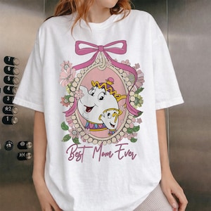 Puede incluir: Camiseta blanca con un marco ovalado rosa que presenta una imagen de dibujos animados de la Sra. Potts y Chip de La Bella y la Bestia, rodeados de flores y un lazo rosa. El texto "Best Mom Ever" está debajo.