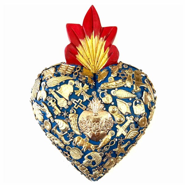 Puede incluir: Un adorno de pared en forma de corazón con una base azul intenso, decorado con numerosos dijes de metal dorado que incluyen cruces, llaves y una calavera. En la parte superior, una cresta en forma de llama roja y dorada sobresale del centro.