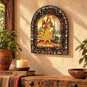 May include: An arched wall plaque featuring a central painting of a winged figure in a yellow robe holding a staff and a fish. The frame is black with intricate, colorful floral patterns and small embossed metallic-toned decorative motifs.
