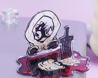 May include: A clear acrylic charm featuring a cartoon illustration of a character in a dramatic scene. The design includes a fallen figure in a pool of red, with a sword and another character looming above. The charm has a glossy finish.