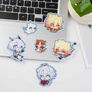 以下が含まれることがあります： 様々なキャラクターが描かれた、鮮やかな色と詳細なデザインのアニメ風ステッカーのコレクション。ステッカーはノートパソコンと白い表面に配置され、背景には植物があります。