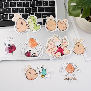 Può includere: Una collezione di adesivi di cartoni animati colorati di varie forme e dimensioni. Gli adesivi presentano personaggi con bordi bianchi. Alcuni raffigurano creature con orecchie da coniglio e altri hanno tratti simili a insetti.