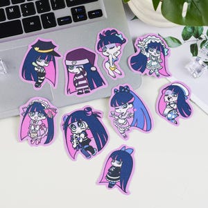 May include: A selection of anime-style stickers depicting characters with long dark blue hair and different outfits. The stickers have a pink border and are on a laptop and a white surface.