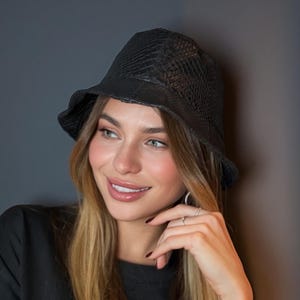 May include: A black bucket hat with a textured, snake-like pattern. The hat is worn with a black t-shirt with white lettering. The shirt has the word "VALENTINA" printed on it.