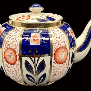 May include: A decorative teapot with a white, blue, and gold design. The teapot features a rounded body with a lid and handle. The design includes blue stripes, floral patterns, and gold accents. The teapot is a vintage item.