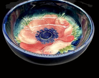 May include: A ceramic bowl with a dark blue exterior and a floral design. The interior features a large pink flower with a blue centre, surrounded by green leaves. The bowl is round and has a glossy finish.