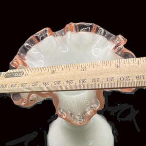 May include: A white and pink ruffled glass pedestal bowl. The bowl has a round base and a flared, ruffled rim. The rim is accented with a pink hue. The bowl's diameter is approximately 4 inches.
