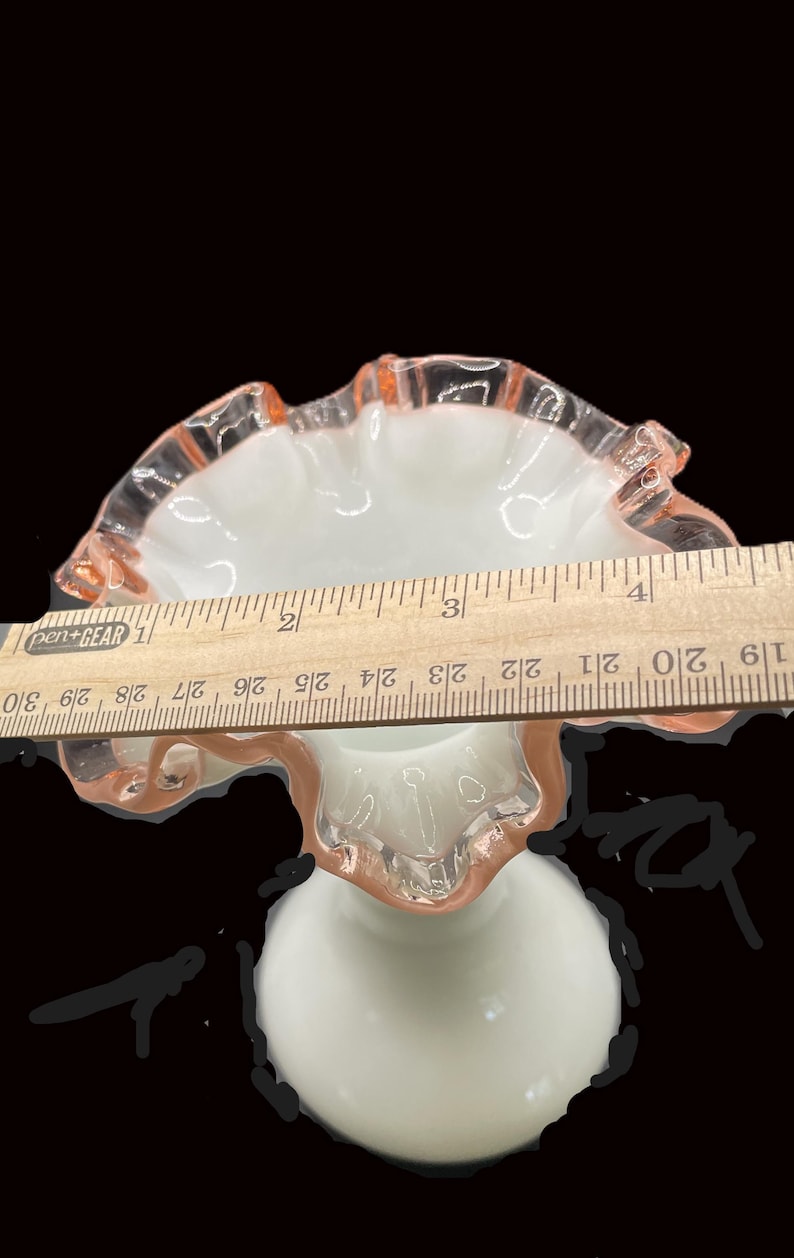 May include: A white and pink ruffled glass pedestal bowl. The bowl has a round base and a flared, ruffled rim. The rim is accented with a pink hue. The bowl's diameter is approximately 4 inches.