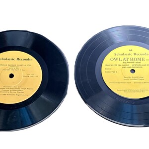 May include: Two vintage vinyl records with yellow labels. One record is titled "Curious George Takes a Job" and the other is "Owl at Home." Both records are black with the "Scholastic Records" logo.