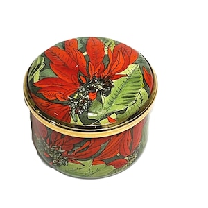 May include: A round, lidded trinket box featuring a vibrant botanical print of red poinsettia flowers and green leaves against a dark background. The container has a polished gold-tone metal rim around the lid and the base of the main body.