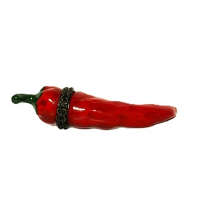 May include: A glossy red chilli pepper figurine with a green stem and a dark metallic band featuring an embossed floral pattern encircling the upper portion of the pepper. The surface of the chilli pepper is smooth and reflective with a curved shape.