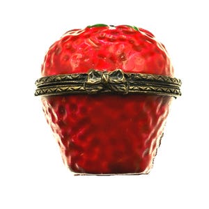 Peut inclure: Une boîte à bijoux en forme de fraise avec une finition rouge brillante et une surface texturée. La boîte présente une ouverture à charnière sécurisée par une bande métallique couleur laiton antique avec un petit fermoir en forme de nœud.