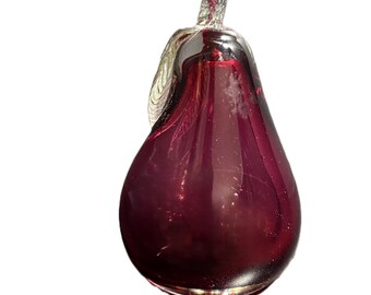 May include: A decorative glass pear in a deep burgundy color. The pear-shaped ornament has a silver-colored stem and leaf detail. The glass is smooth and reflective, with a slight transparency. The pear is a unique home decor item.