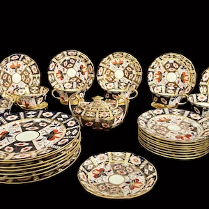 May include: An antique tea set comprising plates, saucers, cups, and a teapot. The set displays a repeating geometric pattern in black, white, red, and gold. The edges of the plates and cups are trimmed with gold.