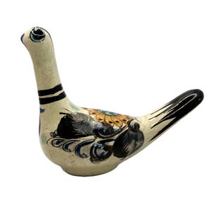 Peut inclure: Une figurine d'oiseau en céramique de couleur blanc cassé, ornée de motifs floraux et de feuilles peints à la main en noir, bleu et orange. L'oiseau présente un long cou avec deux rayures noires, une queue pointue et un œil sombre.