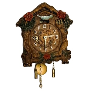 Peut inclure: Une horloge murale marron avec une finition texturée imitation bois, dotée d'un cadran circulaire avec des chiffres blancs de 1 à 12. L'horloge est décorée de fleurs rouges, de feuilles vertes et d'un petit oiseau bleu. Deux poids dorés pendent.