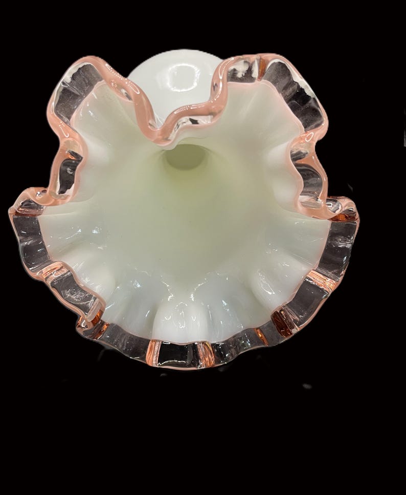 May include: A white glass vase with a ruffled rim, accented with a delicate pink trim. The vase has a flared opening and a smooth, rounded body. The interior has a soft, pale green hue.