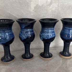 May include: Four handmade ceramic goblets with a dark blue glaze on the rim and base, transitioning to a lighter blue and white speckled pattern in the middle. The goblets have a classic, elegant shape.