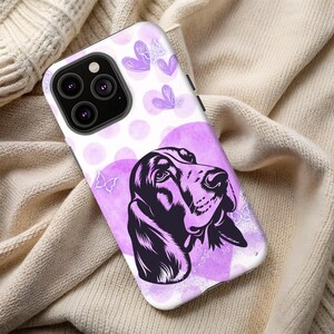 May include: A white phone case featuring a purple and black illustration of a Basset Hound dog. The design includes purple watercolor circles, hearts, and butterfly accents. The case is designed to fit a smartphone.