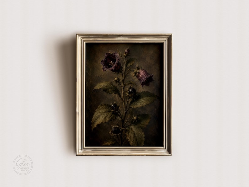 May include: A framed wall art piece featuring a dark, moody botanical illustration of a plant with deep purple bell-shaped flowers and dark green serrated leaves. The artwork is enclosed in a metallic, light-colored rectangular frame.