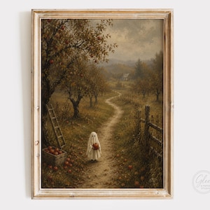 May include: A framed wall art print depicting an autumn orchard scene with a small white ghost figure standing on a dirt path holding a red apple. A wooden ladder leans against a tree near a crate of apples, with a wooden fence along the path.