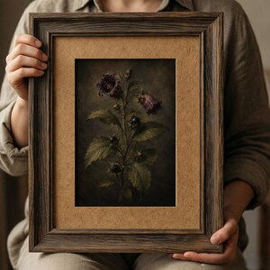 May include: A rectangular dark brown wooden frame containing a botanical print of a dark purple flower with green leaves. The artwork features a moody, shadowed background and is set within a light brown mat board, creating a high-contrast display.