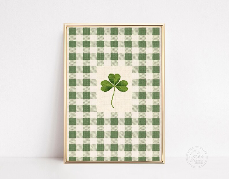 Puede incluir: Impresi&oacute;n enmarcada con un tr&eacute;bol verde sobre un fondo crema, sobre un patr&oacute;n de cuadros verdes y blancos. La obra est&aacute; en un marco dorado, ideal para decoraciones del D&iacute;a de San Patricio. Tama&ntilde;o aproximado: 20 x 30 cm.
