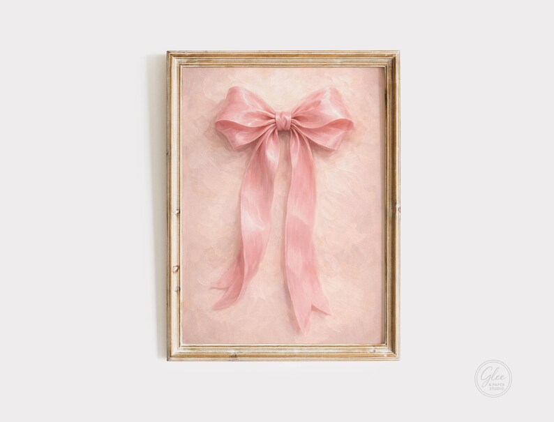May include: A framed print featuring a large, pink bow with long, flowing ribbons. The bow is centered against a textured, light pink background. The frame is a light, distressed gold color, adding a vintage aesthetic.
