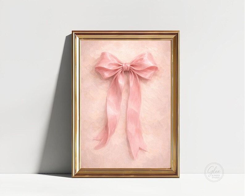 May include: A framed artwork featuring a large, pink bow. The bow is the focal point, set against a soft, textured pink background. The frame is gold-colored, adding a touch of elegance to the piece. The artwork is a decorative item.