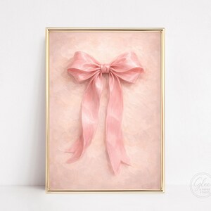 May include: A framed print featuring a large, pink bow with long, flowing ribbons. The bow is the focal point, set against a soft, textured background. The frame is gold. The print is from Glee Paper Studio.
