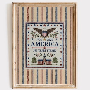 Może przedstawiać: Oprawiony haft krzyżykowy przedstawiający bielika amerykańskiego, budynek w stylu kolonialnym oraz napis "AMERICA 1776 2026 250 YEARS STRONG" otoczony niebieskimi i czerwonymi gwiazdami. Tło stanowi tkanina w pionowe czerwone, białe i niebieskie paski.