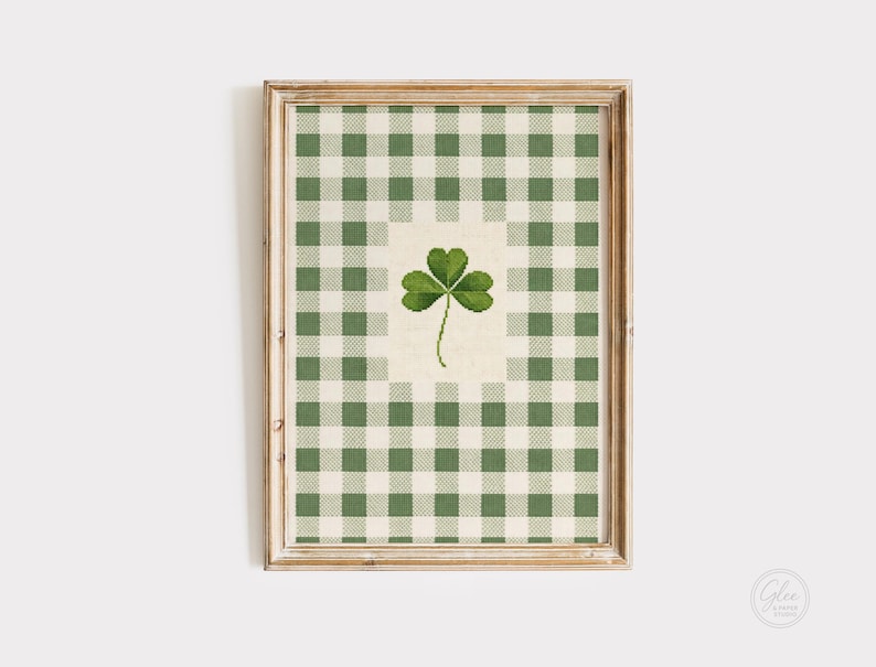 Puede incluir: Arte de pared enmarcado con un fondo de patr&oacute;n de cuadros verdes y blancos y un tr&eacute;bol en el centro. El tr&eacute;bol es de color verde vibrante, sobre un fondo crema. El marco es de madera clara, a&ntilde;adiendo un toque r&uacute;stico.