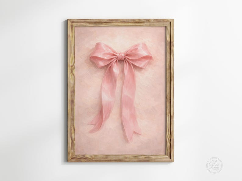 May include: A framed print featuring a large, soft pink bow with long, flowing ribbons. The bow is centered on a light pink, textured background. The wooden frame adds a rustic touch to the artwork.