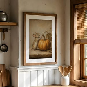 Peut inclure: Une impression d'art murale encadr&eacute;e repr&eacute;sentant une peinture d'une petite souris debout &agrave; c&ocirc;t&eacute; d'une grosse citrouille orange. L'&oelig;uvre est pr&eacute;sent&eacute;e dans un cadre en bois et accroch&eacute;e sur un mur de cuisine blanc, entour&eacute;e d'ustensiles.