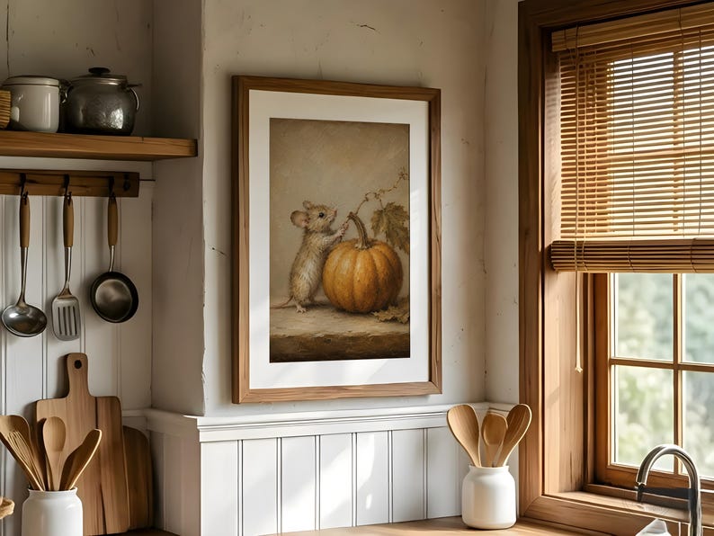 Peut inclure: Une impression d'art murale encadr&eacute;e repr&eacute;sentant une peinture d'une petite souris debout &agrave; c&ocirc;t&eacute; d'une grosse citrouille orange. L'&oelig;uvre est pr&eacute;sent&eacute;e dans un cadre en bois et accroch&eacute;e sur un mur de cuisine blanc, entour&eacute;e d'ustensiles.