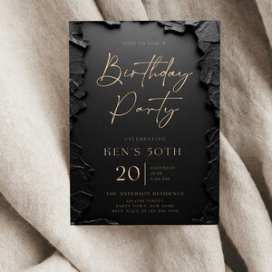 May include: A rectangular birthday party invitation card with a matte black center and textured, jagged black edges. The text is printed in gold, featuring the words Birthday Party, Ken's 50th, 20 Saturday June 7:00 PM, The Anderson Residence, 123 Oak Street, Party Town, New York, and RSVP Alice at 123-456-7890.