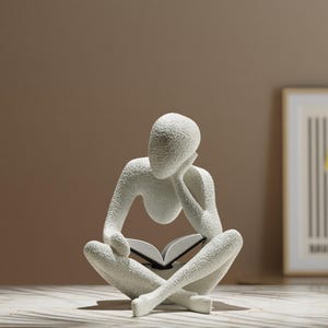 Könnte beinhalten: Eine weiße, strukturierte Skulptur einer Person, die ein Buch liest und im Schneidersitz sitzt. Die Figur befindet sich in einer nachdenklichen Pose, mit dem Kopf auf der Hand. Diese dekorative Skulptur eignet sich für die Inneneinrichtung.