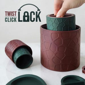 Könnte beinhalten: Ein Set aus zylindrischen Behältern mit einem dunkelroten und dunkelgrünen geometrischen Muster. Der Text TWIST CLICK LOCK mit einem Vorhängeschloss-Symbol ist sichtbar. Die Behälter haben ein modulares Design mit separaten Deckeln.